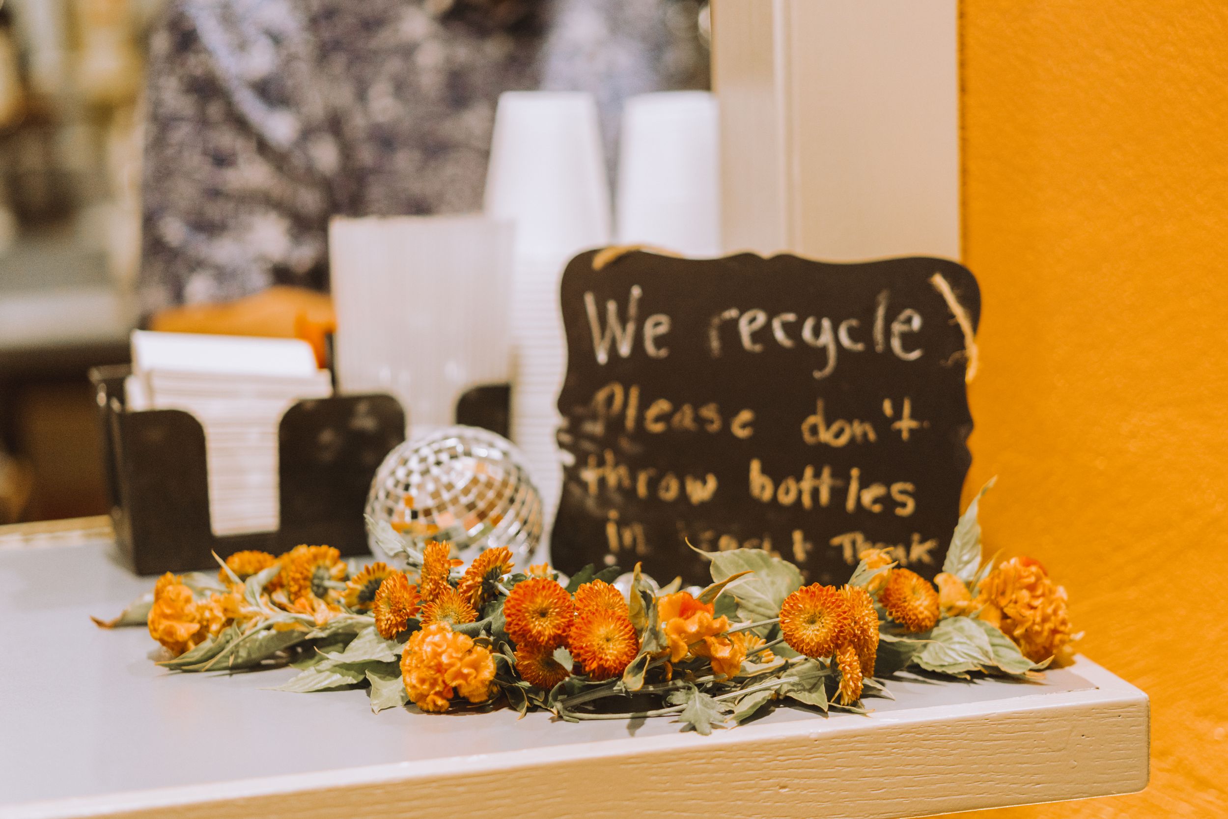 Chalkboard sign about recycling with orange flowers and disco ball decorations.