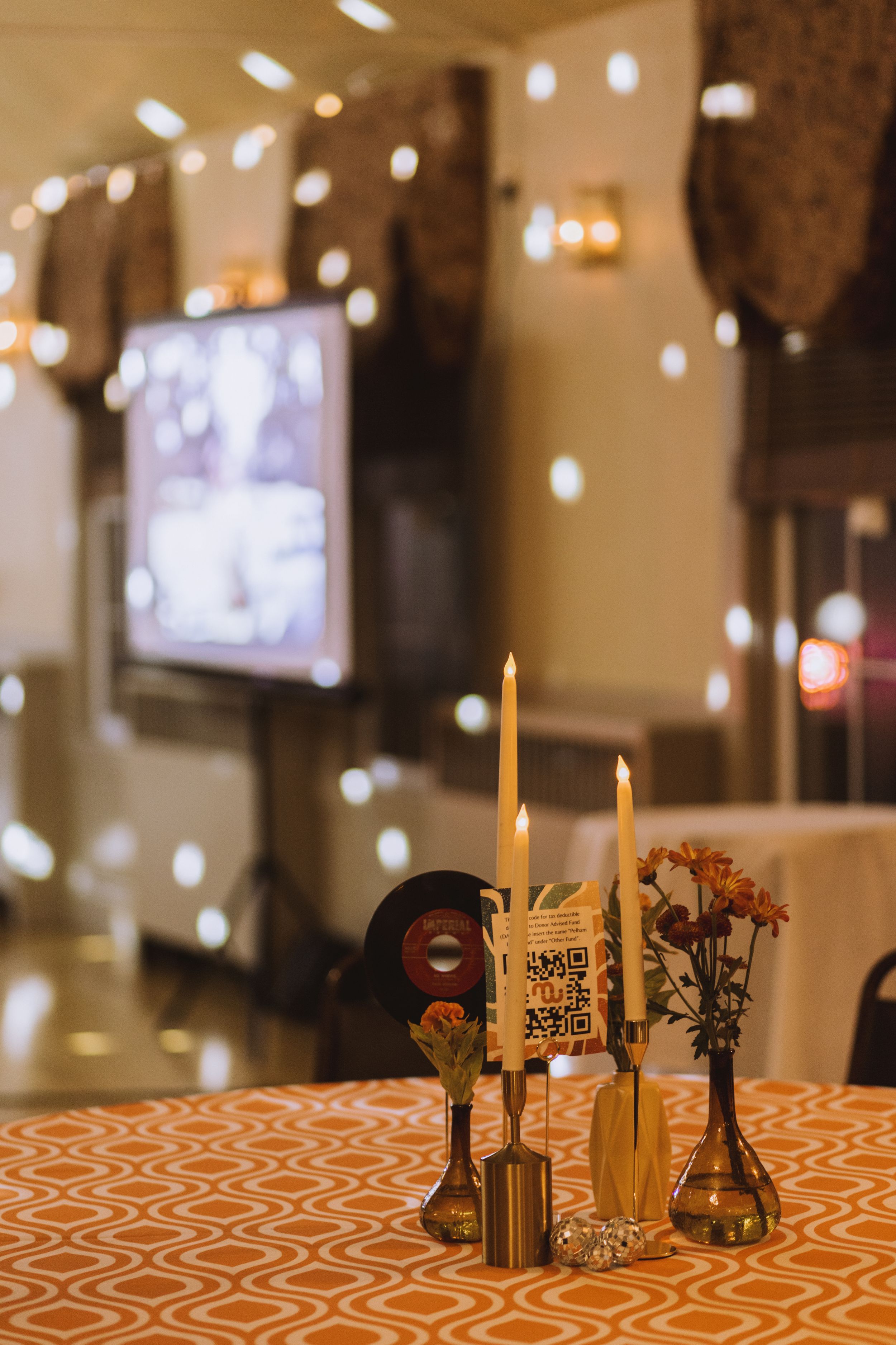 Table centerpiece with tall candles, flowers, and vinyl records on an orange geometric patterned tablecloth.