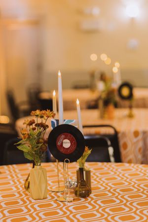 Vintage record and taper candle centerpiece with orange flowers on a geometric print tablecloth.