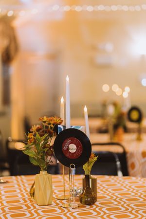 Close-up of wedding table centerpiece featuring vinyl record, white candles, and orange flowers.