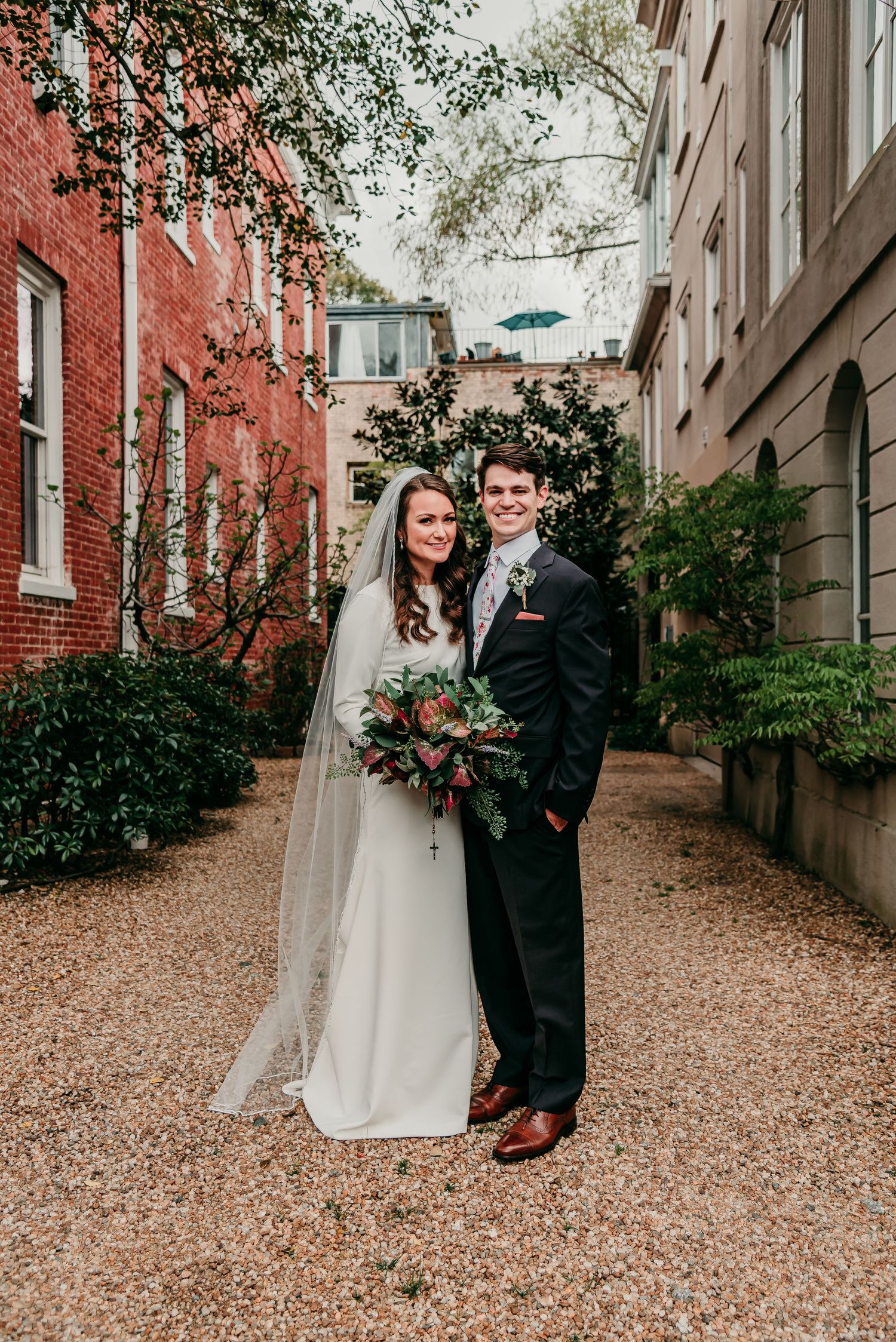 Wedding couple poses in a charming alleyway between red brick and stone buildings.