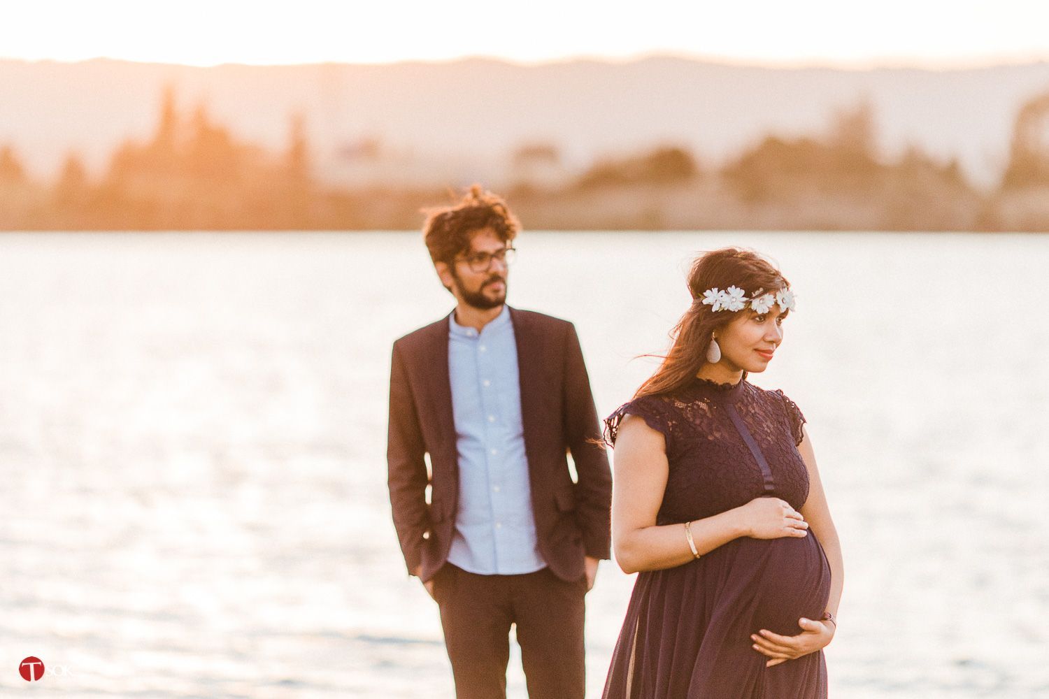A romantic sunset maternity photo shoot by the water with warm golden light.
