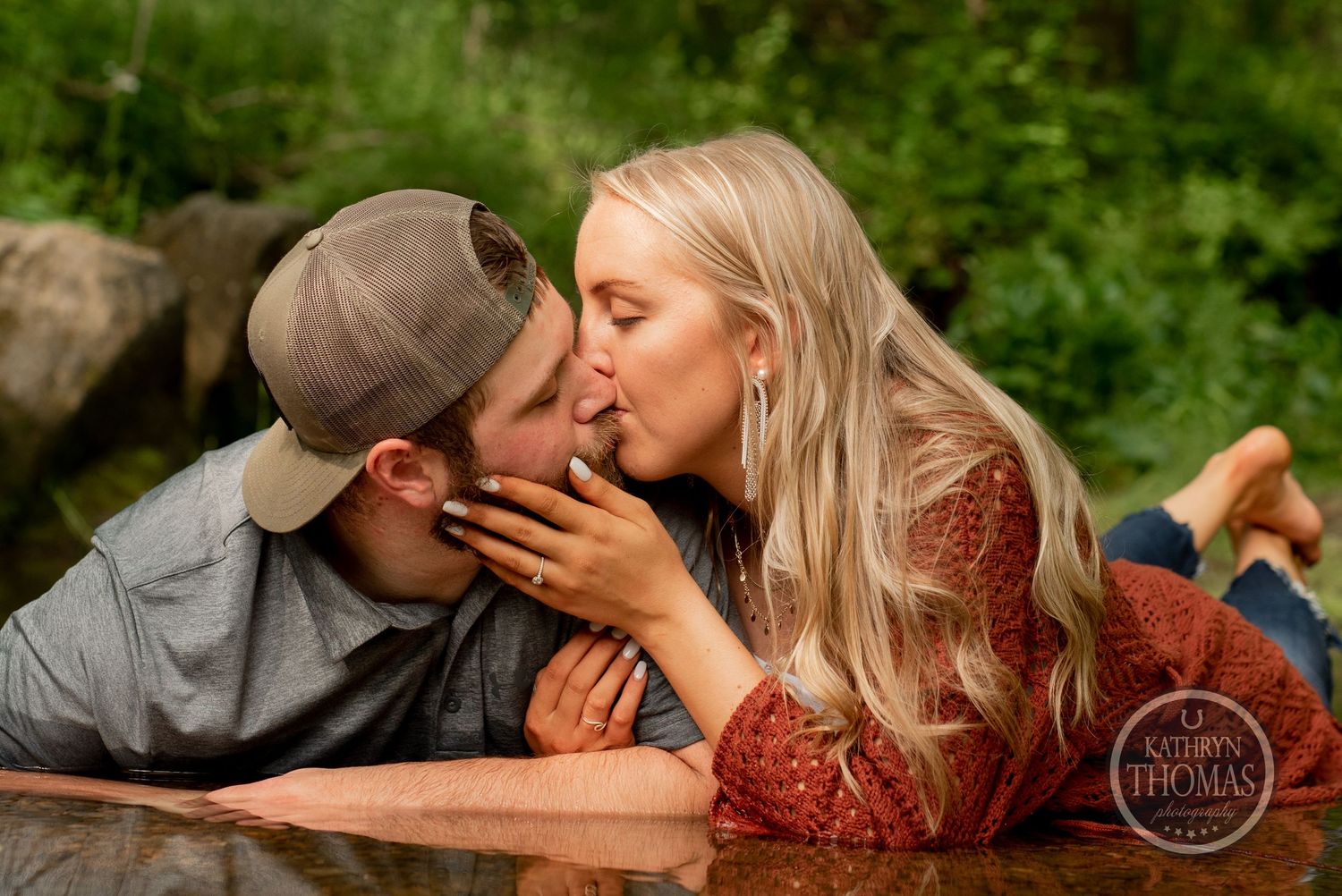 A romantic moment captured between two people lying on ground in a natural outdoor setting.