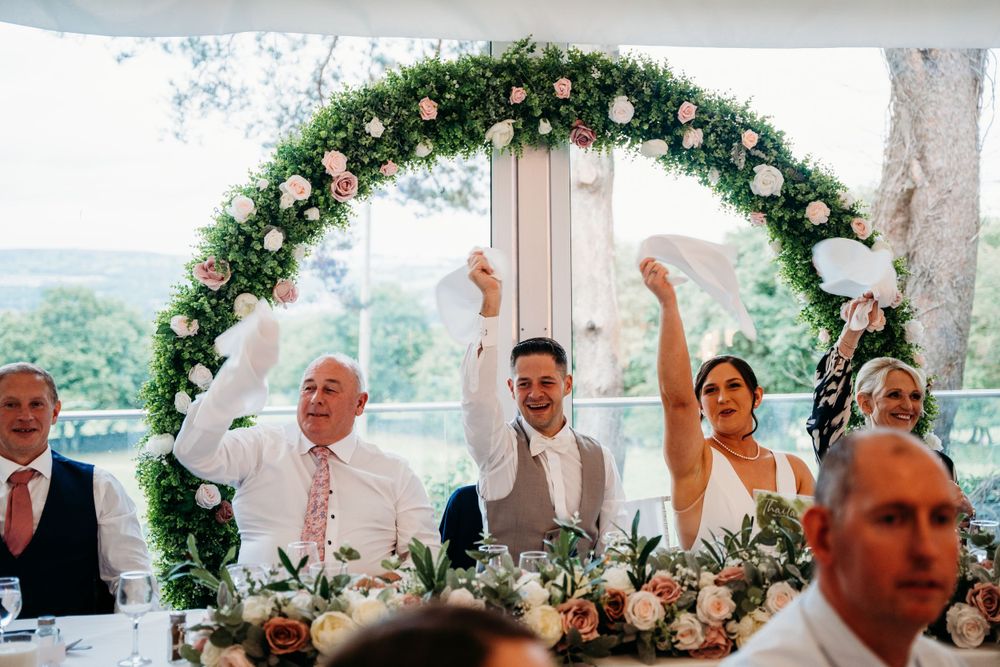 A wedding reception table under a floral arch with white and pink roses.