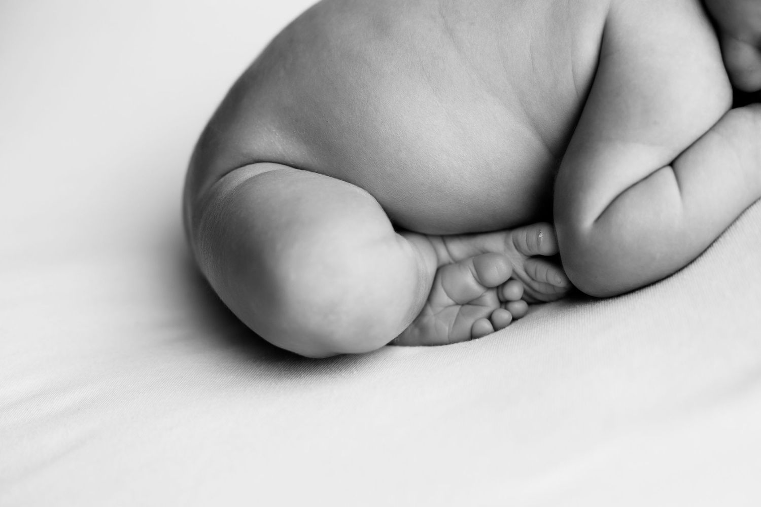 Newborn baby boy on a white backdrop.  This is a close up of his ankles crossed and toes showing.