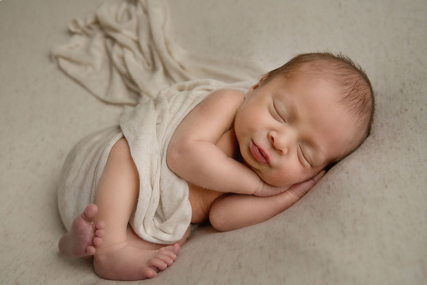 Peaceful sleeping newborn baby wrapped in soft white fabric during studio photography session.