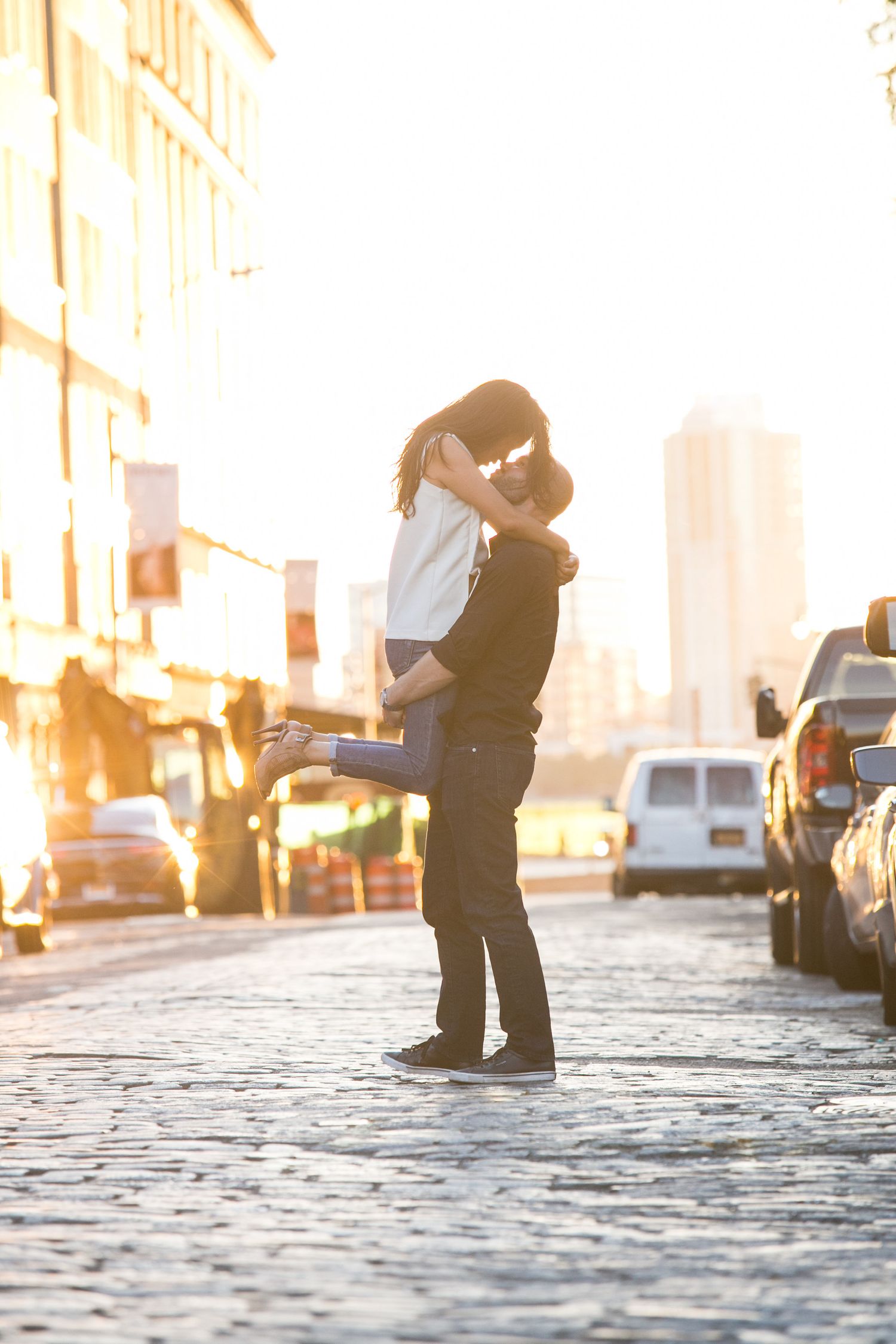 A romantic silhouette of a couple embracing on a cobblestone street at sunset.