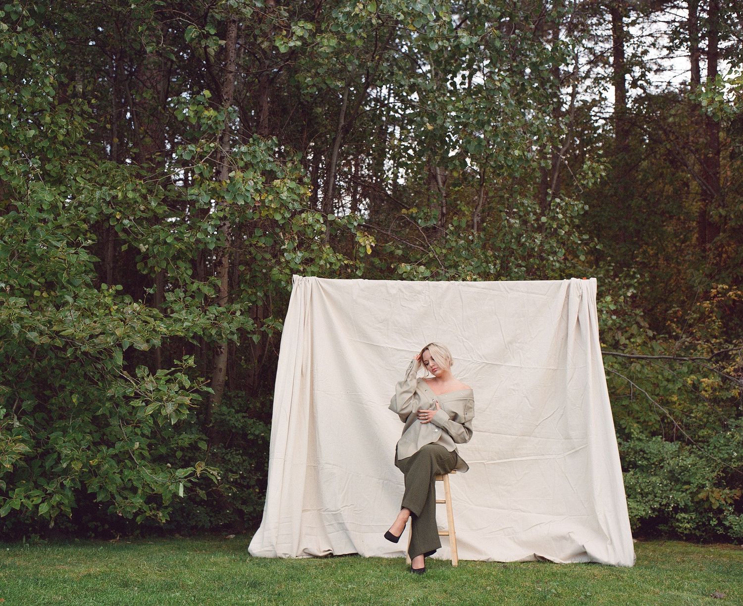 Outdoor editorial portrait in Kelowna on stool in front of backdrop, featuring natural glam makeup and soft photography by Brianne Bennett