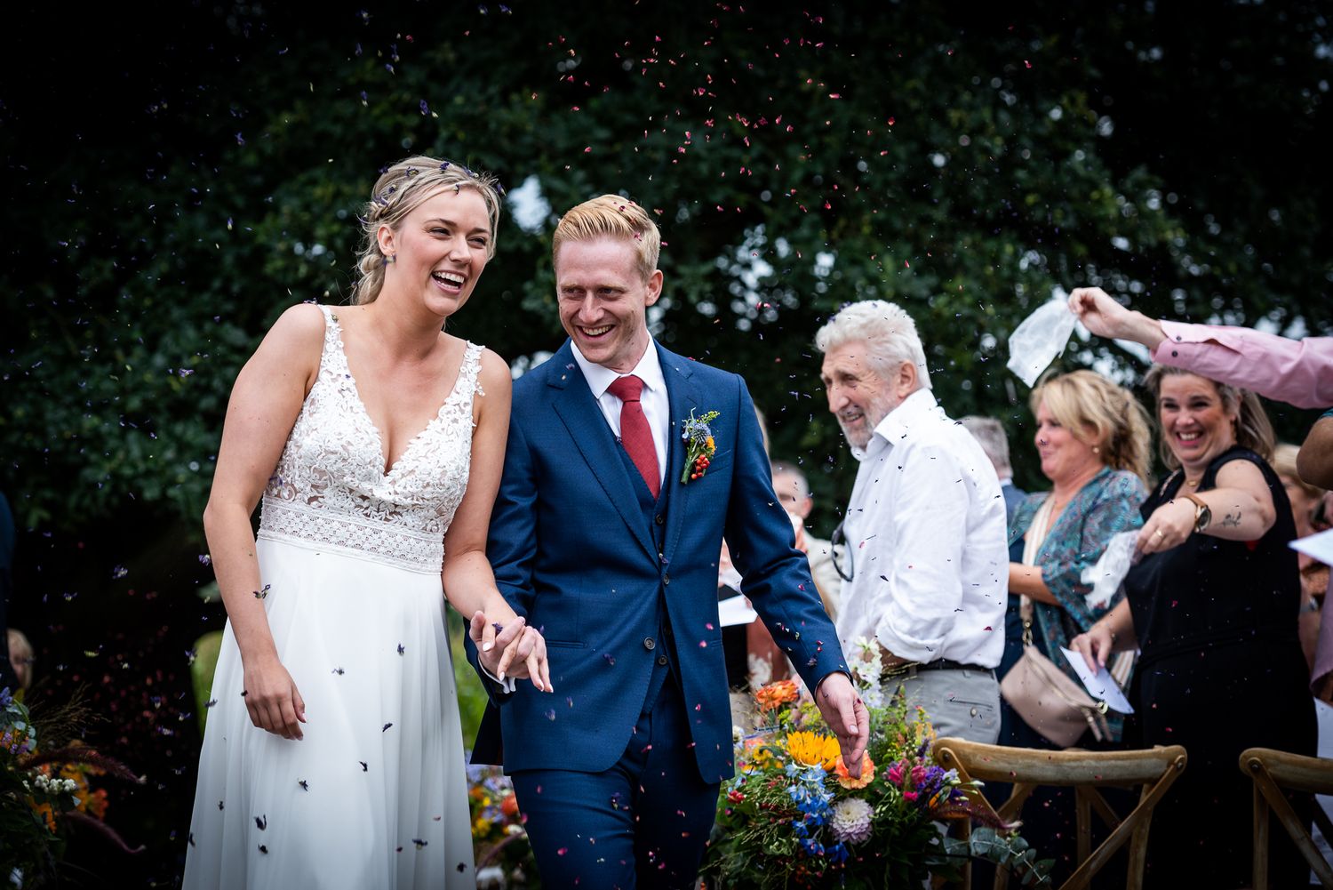 Bruidspaar verlaat de ceremonie terwijl de gasten hen met bloemen confetti bekogeleni