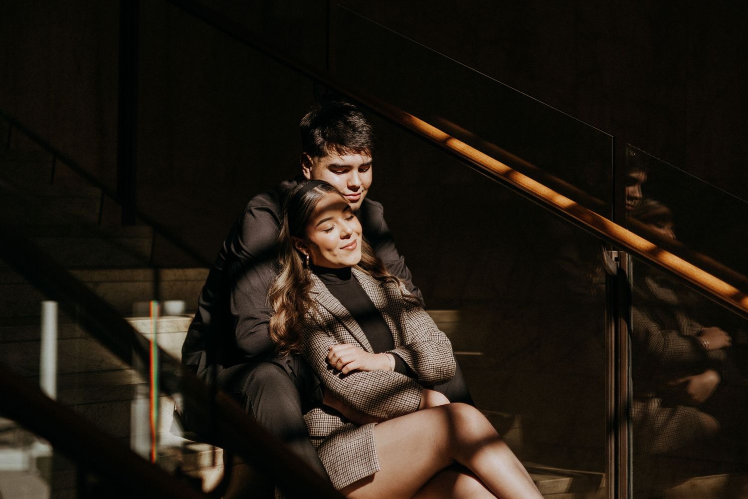 Two people share a tender moment while sitting on dark wooden stairs.