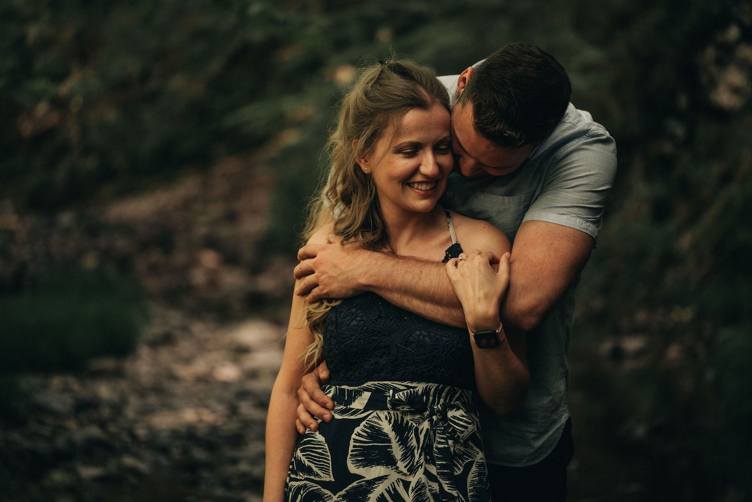 A tender embrace captured in warm natural lighting against a forest backdrop.