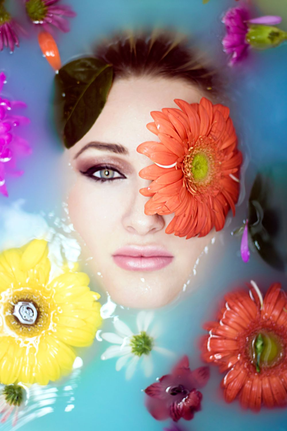 Ethereal beauty shot surrounded by orange, yellow and pink flowers in water.