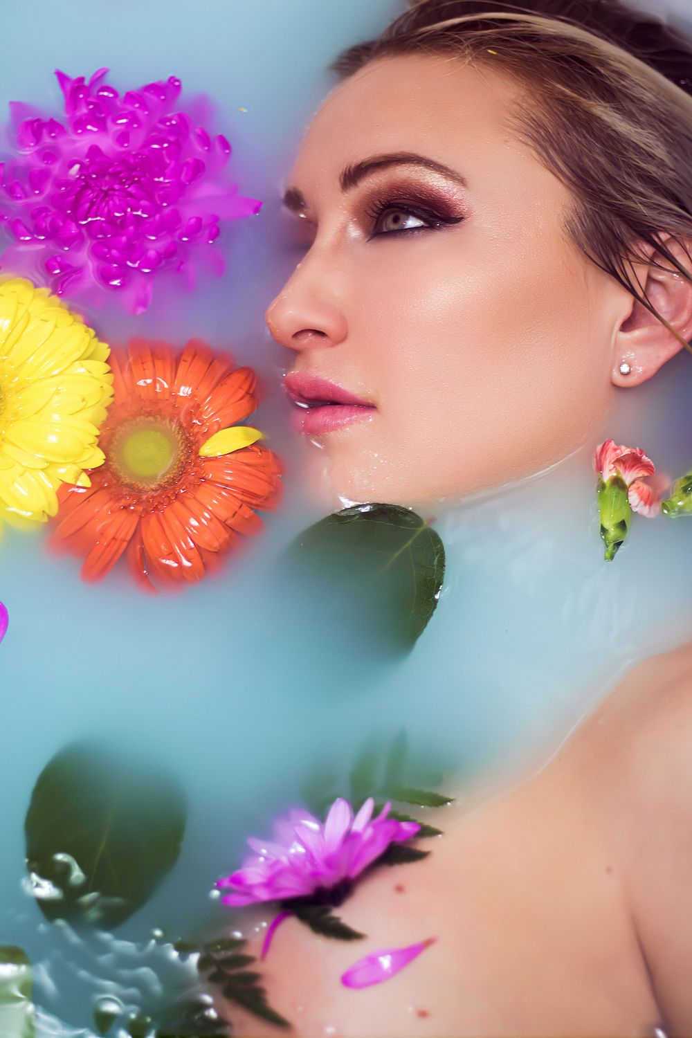 Beauty portrait with floating gerbera daisies and soft turquoise background.