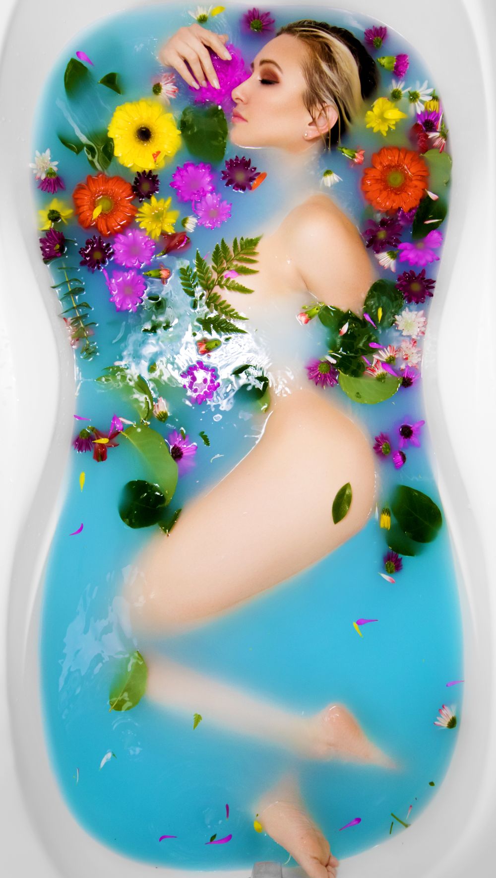 Artistic bathtub portrait with vibrant floating flowers and turquoise water creating dreamy atmosphere.