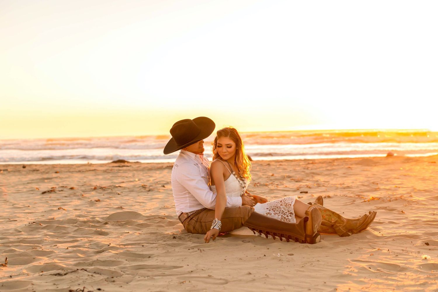 Happy couple sitting together on a sandy beach at sunset enjoying a romantic moment.