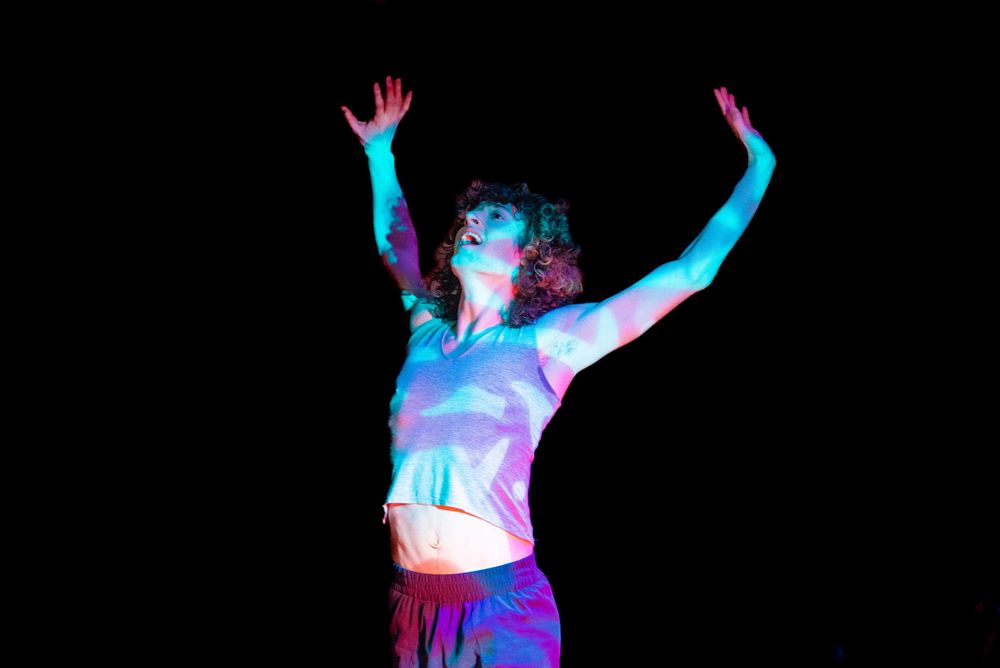 Silhouettes of dancers performing with colorful neon lighting effects against a dark background.