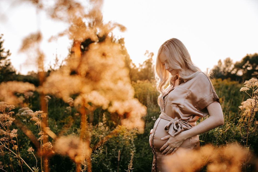 Peaceful maternity photo among wildflowers at sunset with soft lighting.