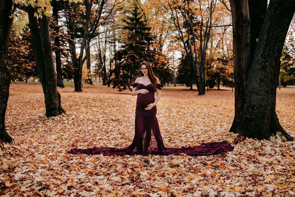 Dramatic maternity photo in purple dress surrounded by autumn leaves.