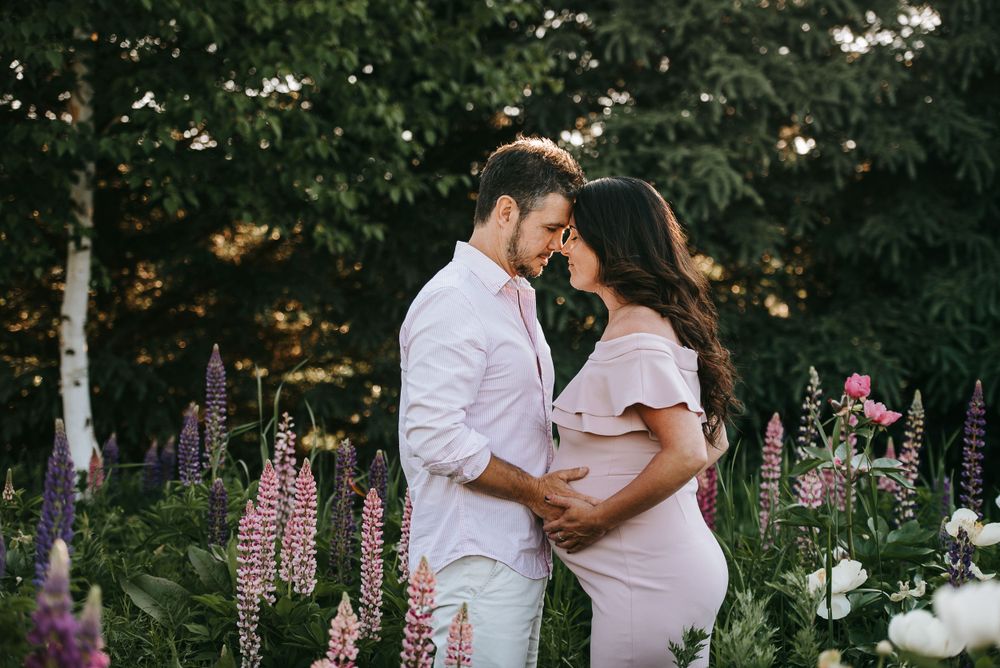Romantic maternity photos with pink lupine flowers in a garden setting at sunset.
