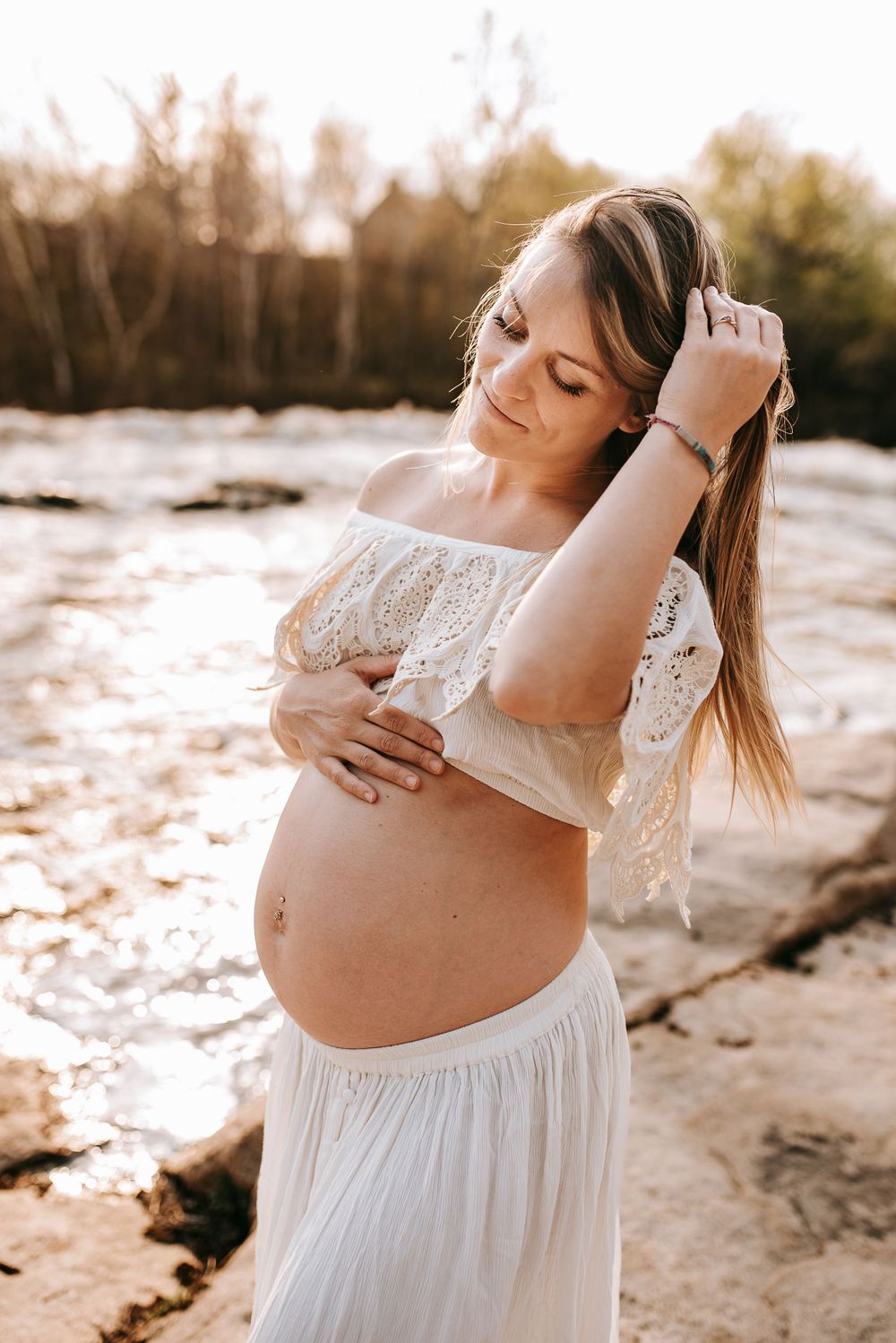 Maternity portrait on rocky terrain with white lace dress during sunset.