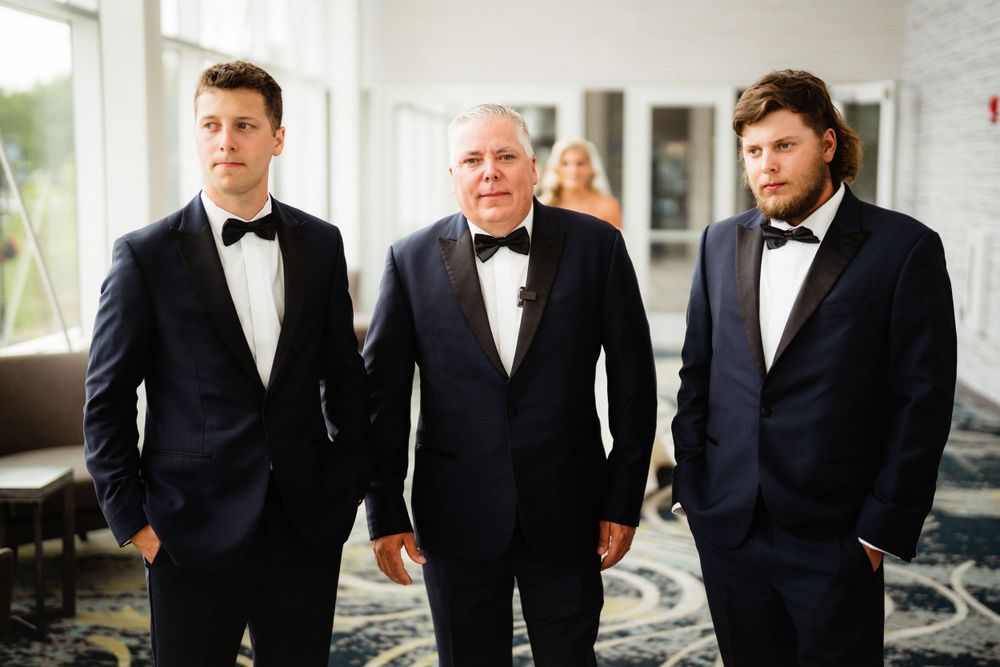 Three men in black tuxedos stand together at formal event.