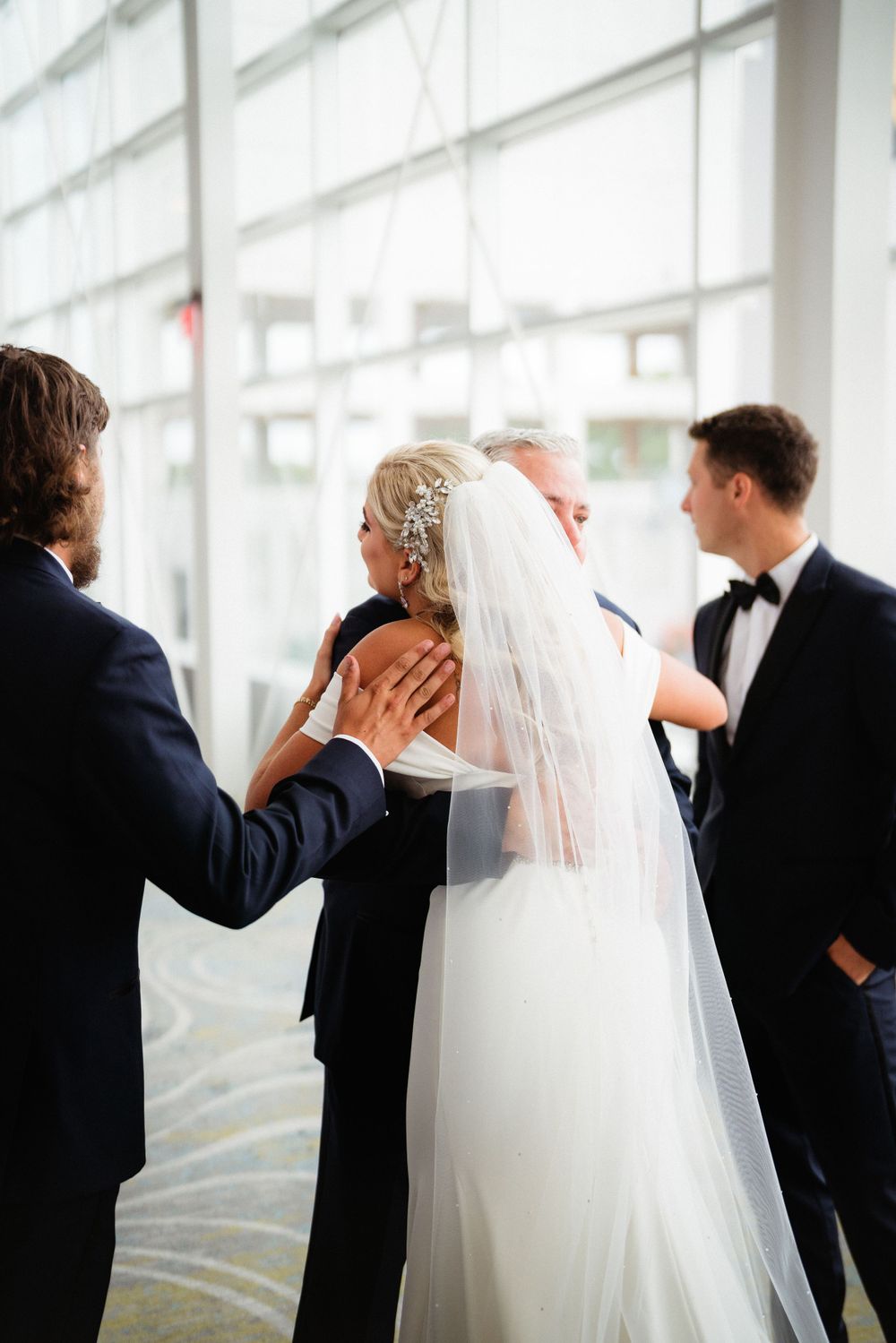 An intimate wedding moment shared between loved ones in a bright corridor.