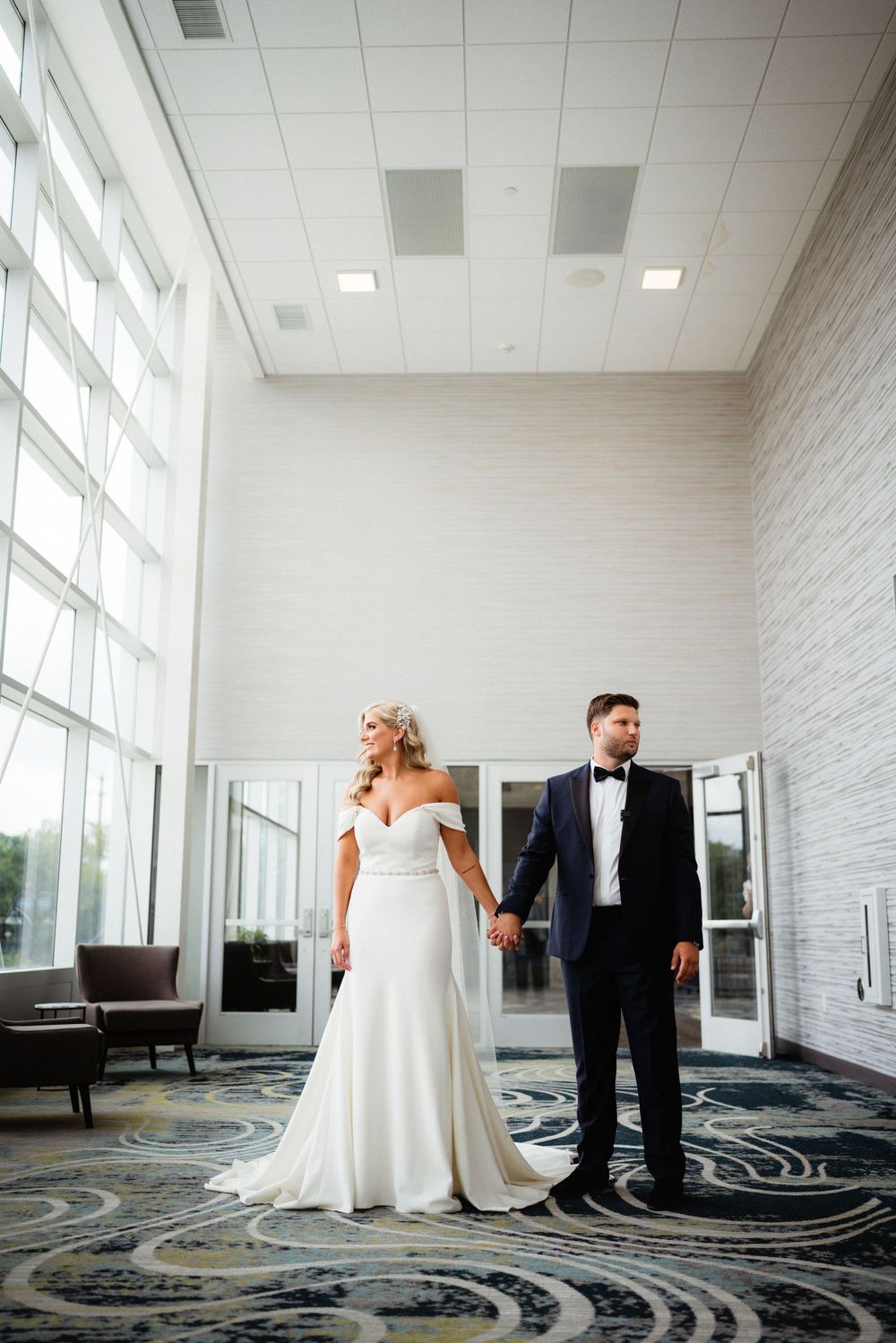 A formal wedding portrait in an elegant hallway with large windows and modern decor.