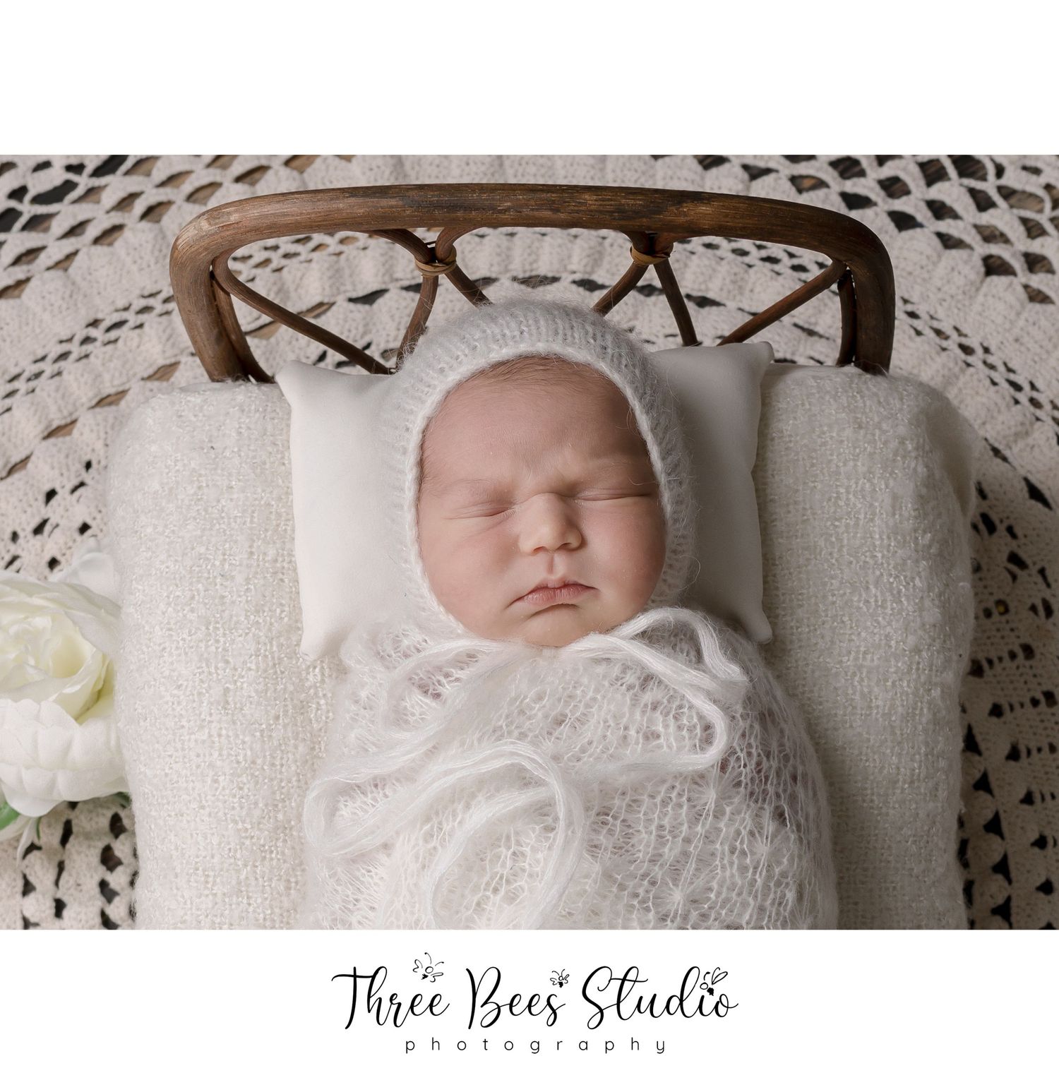 Newborn resting on white lace blanket in vintage-style basket setting.