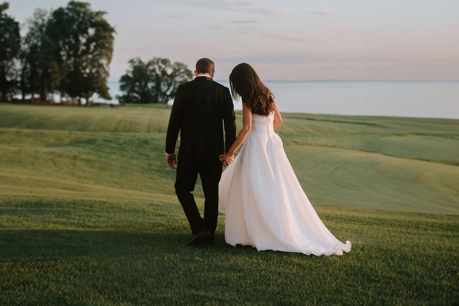 Couple walking together on golf course at sunset, bride in flowing white dress.