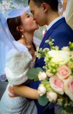 Tender wedding kiss moment captured with soft focus and pink roses in the foreground.