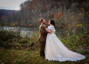 A couple shares a romantic moment in their wedding attire against an autumn landscape backdrop.