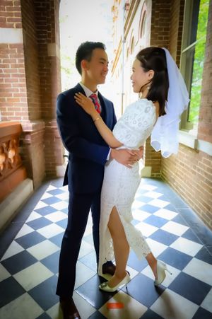 Bride and groom share intimate dance pose on checkered floor with brick wall background.
