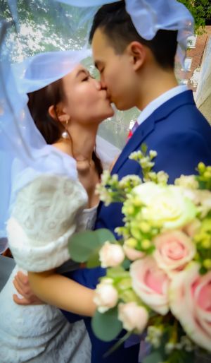 A tender wedding kiss moment with pink roses in the foreground and natural greenery in the background.