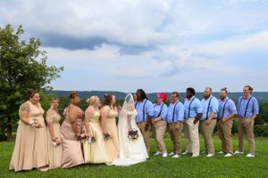 Wedding party in peach dresses and blue shirts poses on hilltop with scenic view.