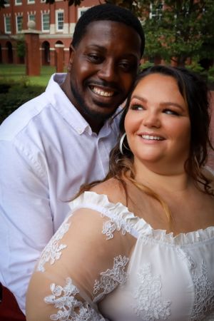 A joyful wedding couple poses together outdoors against a brick building backdrop.