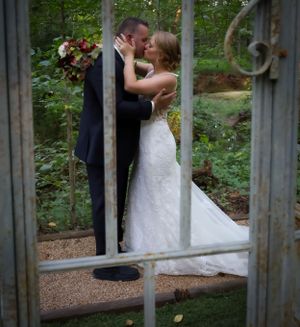 Newlyweds share intimate kiss through garden gate window frame.