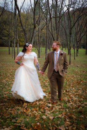 A couple playfully interacts among fallen autumn leaves in a wooded setting.