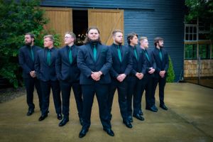 Groomsmen in black suits lined up outdoors for a wedding photo shoot.