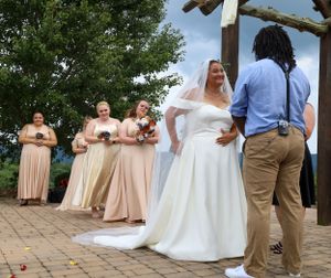 Wedding party poses on stone patio with wooden pergola against scenic mountain backdrop.
