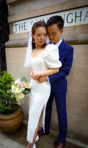 A romantic wedding couple embraces outside The Cunningham building with the bride holding a floral bouquet.