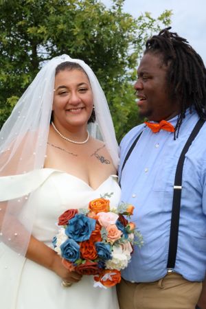 Joyful wedding couple with blue and orange bouquet outdoors.