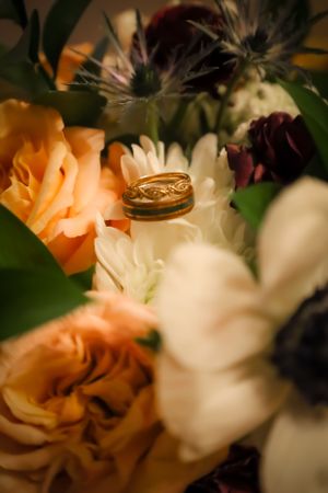 Close-up of delicate peach and white flowers with wedding rings in soft focus.