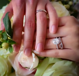 Close-up of engagement ring and wedding band with white roses in background.