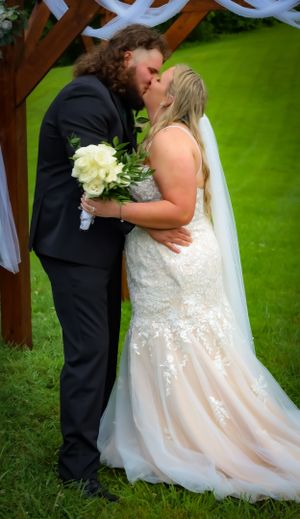 A romantic wedding moment captured under a decorated outdoor pergola with green background.