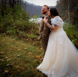 Wedding couple poses together on a scenic wooded hillside during fall.