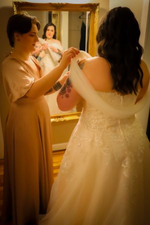 Behind-the-scenes moments of wedding dress preparation in warm lighting.
