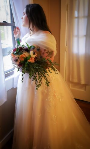 Wedding dress detail with orange and pink floral bouquet by a window.