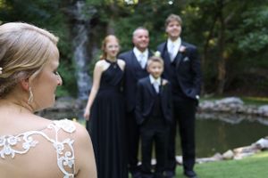 Bride's detailed lace back dress with wedding party standing in background.
