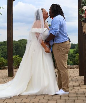 Elegant white wedding dress and veil flows against stone patio during outdoor ceremony.