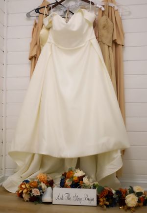White wedding dress hanging against white wall with floral decorations below.